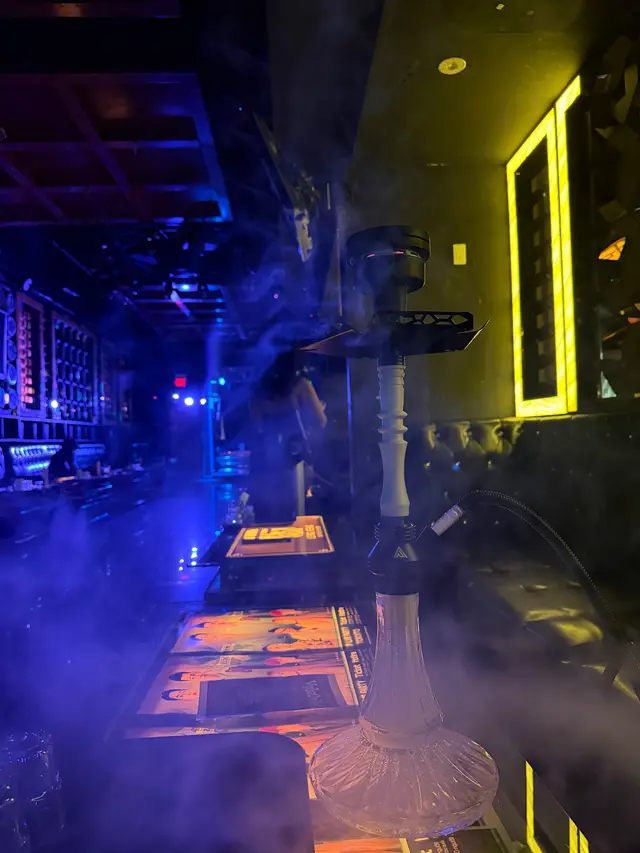 Hookah running on a lounge bar under coloured neon, a thick plume across the room