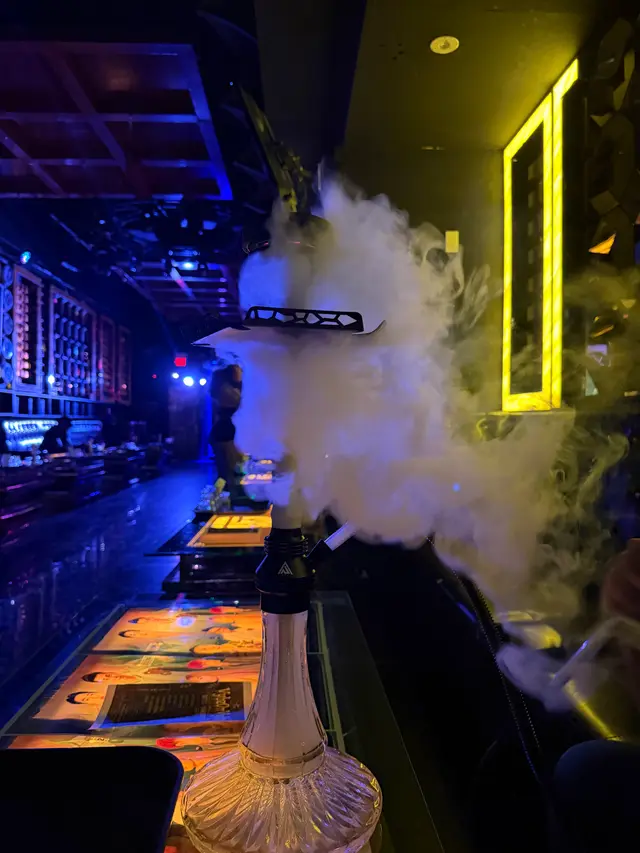 Hookah running on a lounge bar under coloured neon, a thick plume across the room