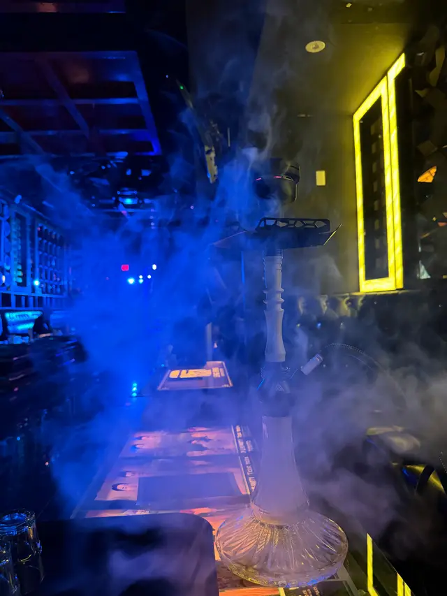 Hookah running on a lounge bar under coloured neon, a thick plume across the room