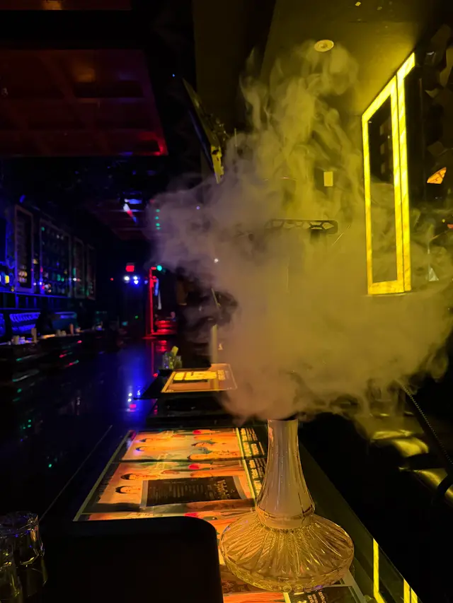 Hookah running on a lounge bar under coloured neon, a thick plume across the room
