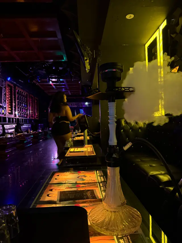 Hookah running on a lounge bar under coloured neon, a thick plume across the room