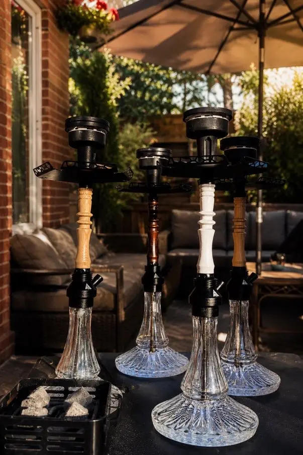 Four hookahs set up under a patio umbrella in a back garden