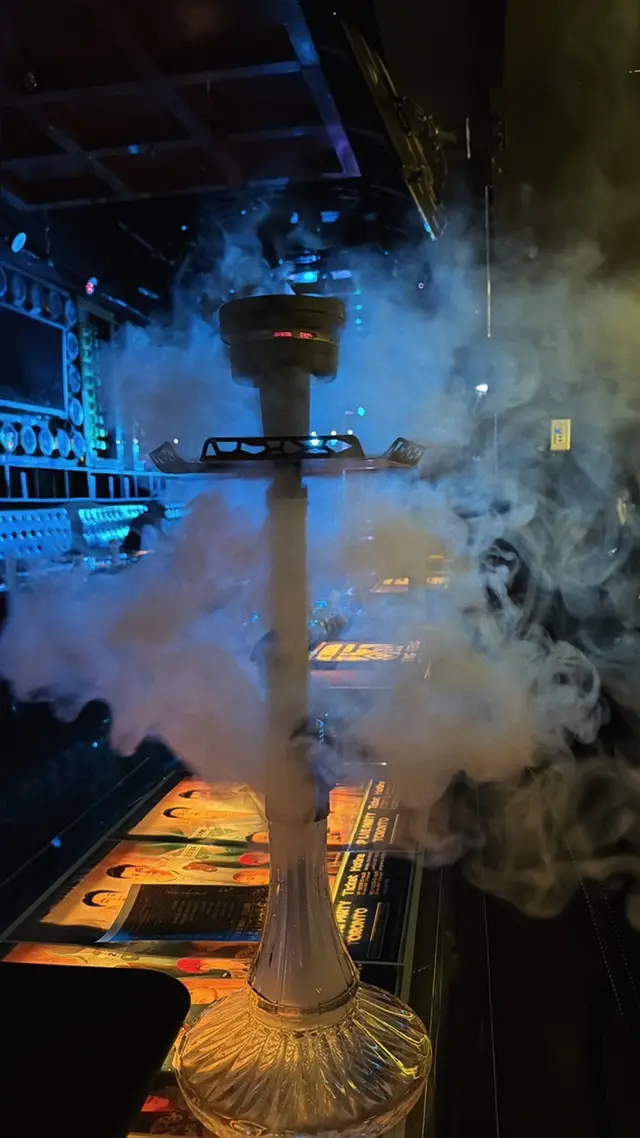 Hookah running on a lounge bar under coloured neon, a thick plume across the room