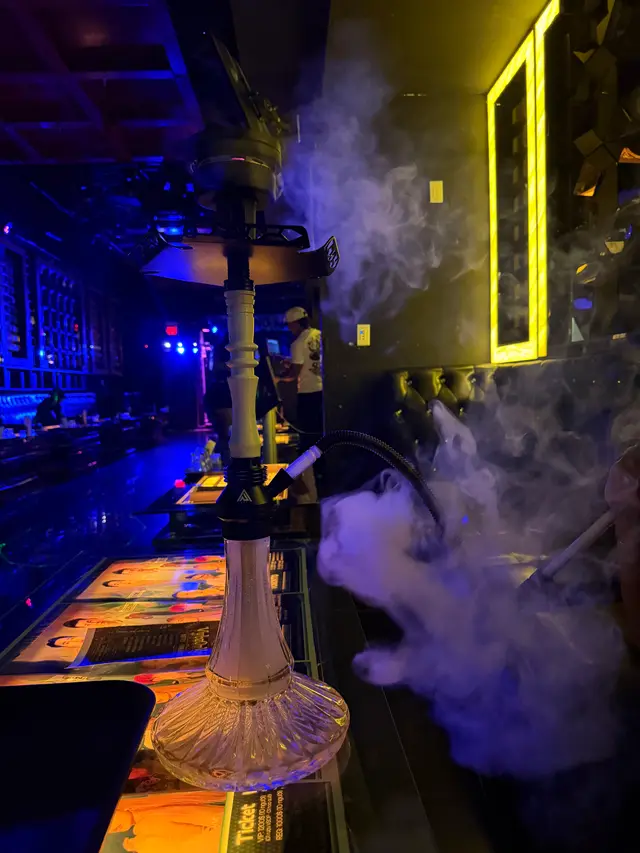 Hookah running on a lounge bar under coloured neon, a thick plume across the room