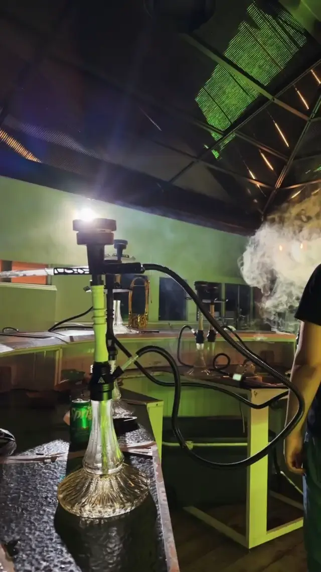 Hookah running under green light, smoke filling the frame